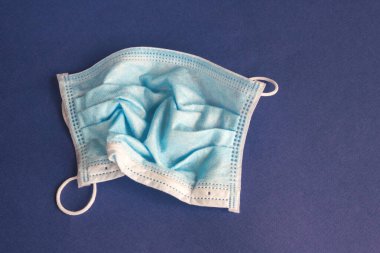 Buruşuk, mavi arka planda tıbbi koruyucu maske kullanılmış. Karantinayı bırakma ve tıbbi maskelerin toplu kullanımı.