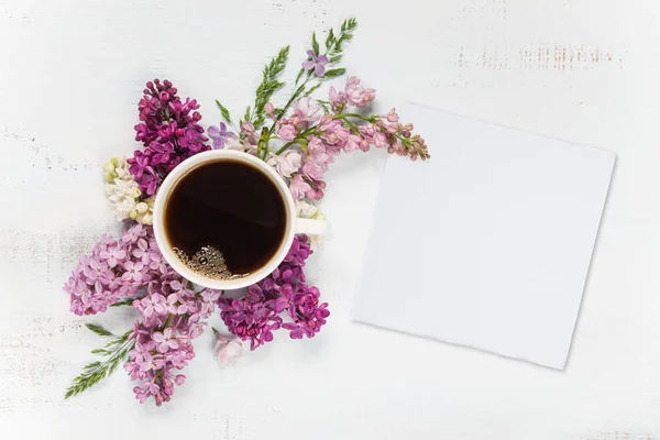 Café, diferentes flores lila y tarjeta de papel blanco — Foto de Stock