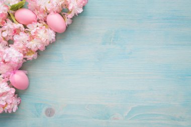Mavi ahşap arka planda pembe çiçekler ve yumurtalar var.