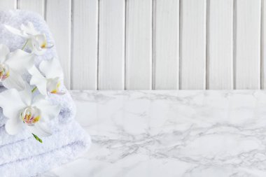 Beyaz havlu yığını ve beyaz orkide çiçekleri mermer bir yüzey üzerinde, tahta kaplamaların beyaz bir zeminine karşı, fotokopi alanı ile