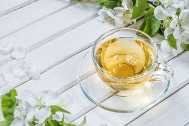 Şeffaf cam çay fincanı ve beyaz ahşap eski püskü arka planda elma ağacı çiçekleri.