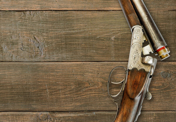 Vintage double barrel hunting gun with shells close-up on an old grunge dark brown wooden background, with copy-space