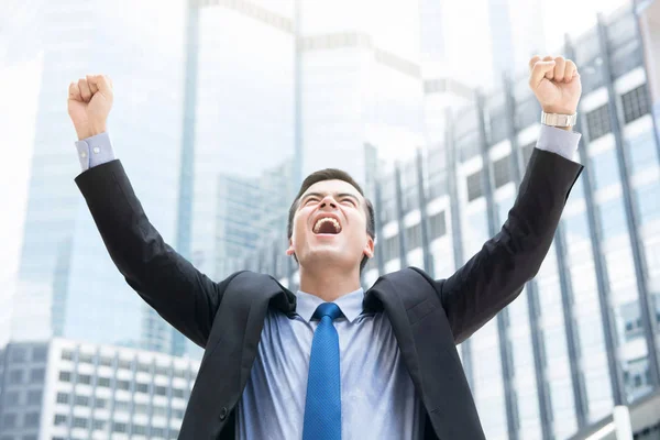 Бізнесмен піднімає кулаки в повітрі на розмитій будівлі офісу — стокове фото
