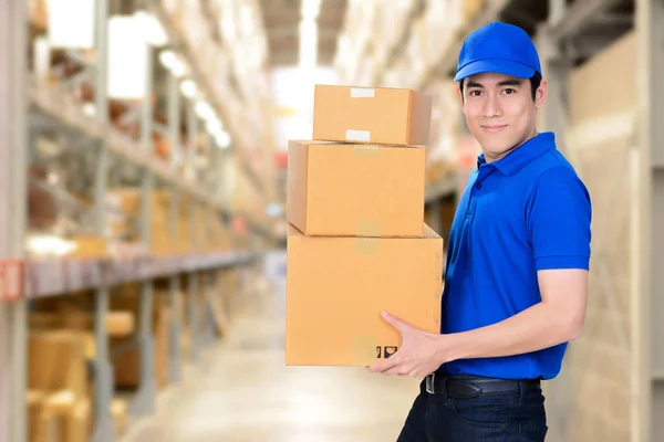 Repartidor sonriente llevando cajas sobre fondo borroso del almacén — Foto de Stock