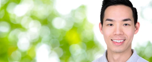 Sonriente joven asiático hombre en abstracto bokeh verde backgr panorámica — Foto de Stock