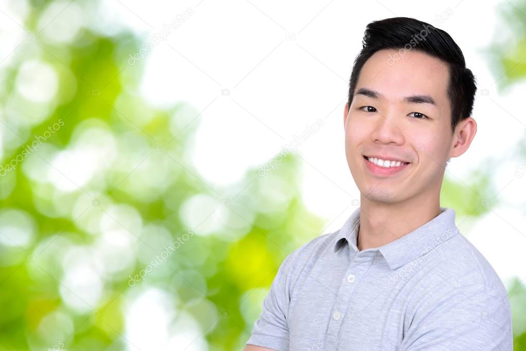 Happy smiling young Asian man on bokeh green abstract background