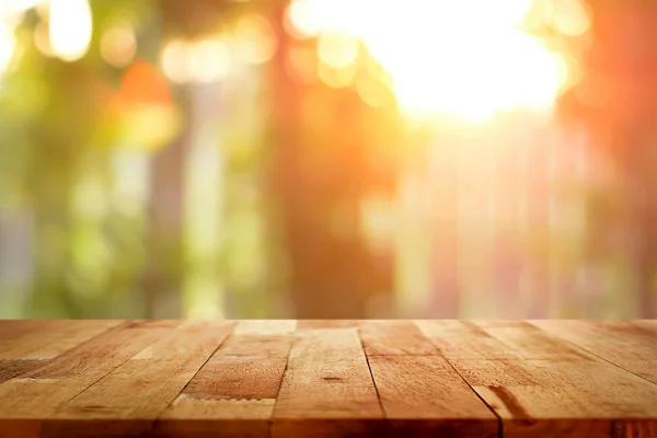 Holztischplatte auf verschwommenem Bokeh-Hintergrund des Sonnenlichts, das durch die Bäume scheint — Stockfoto