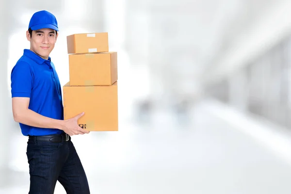 Sorrindo amigável entregador carregando caixas de encomendas no fundo branco borrão — Fotografia de Stock