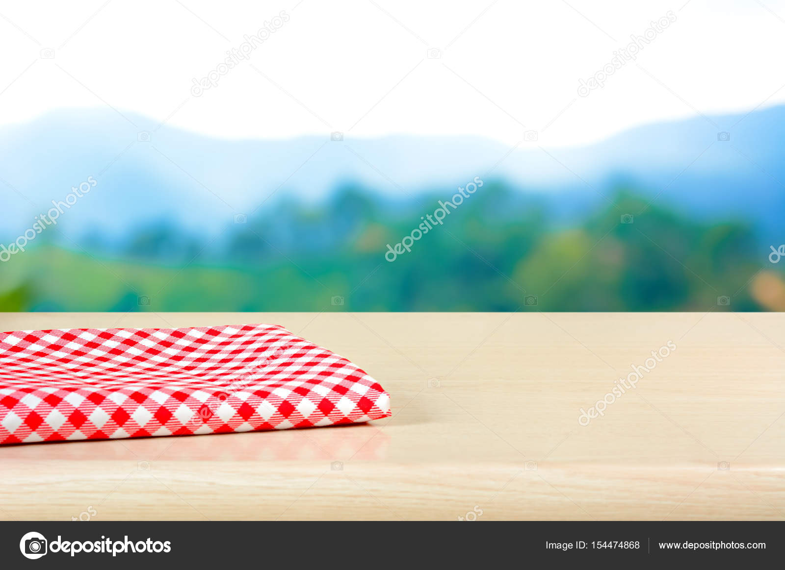 Red checkered cloth on wood table top in blur mountain background
