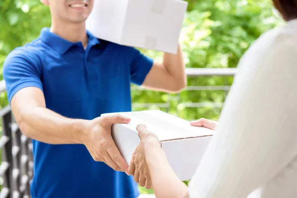 Pria pengantar senyum dengan seragam biru mengantarkan kotak paket kepada seorang wanita — Stok Foto