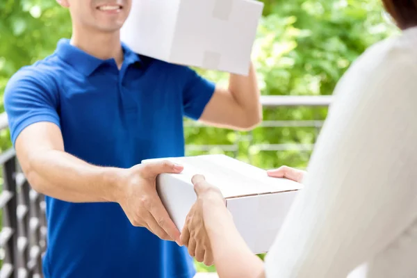 Lächelnder Zusteller in blauer Uniform liefert Paketkasten an Frau aus — Stockfoto