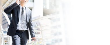 İş adamı cep telefonundan arıyor. Bagajı çekerken ve açık havada yürürken, panoramik afiş ve fotokopi alanı var.