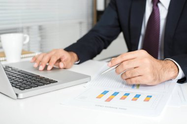 Dizüstü bilgisayar ve masadaki belgeleri ile ofiste çalışan iş adamı