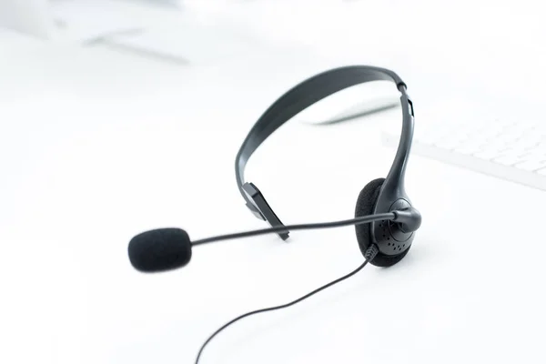 Microfoon headset op witte tafel met computer toetsenbord achtergrond wazig — Stockfoto