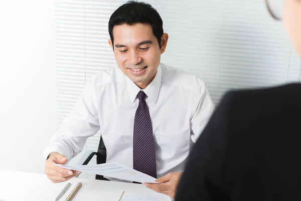 Glimlachend zakenman lezen (controleren) document achter zijn Bureau in het kantoor — Stockfoto