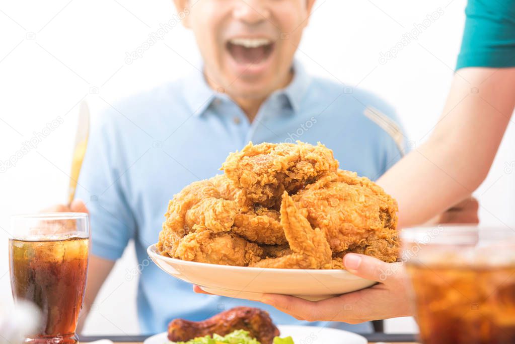 Waiter putting fried chicken on the table in front of young man 