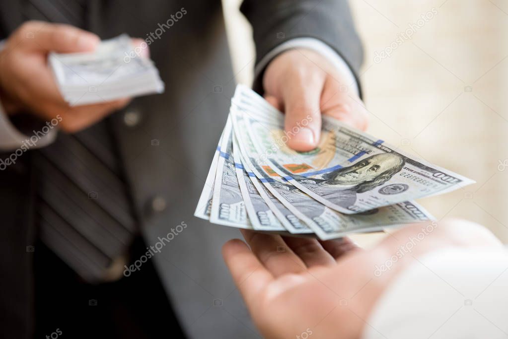 Businessman giving (or paying) money to a man, US dollar bills - loan, bribery and financial concepts