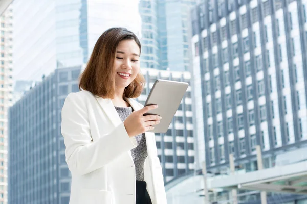 Asiática mujer de negocios utilizando tableta ordenador al aire libre en desenfoque offic —  Fotos de Stock