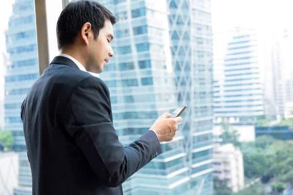 Zakenman met behulp van de mobiele telefoon naast kantoorgebouw venster in — Stockfoto