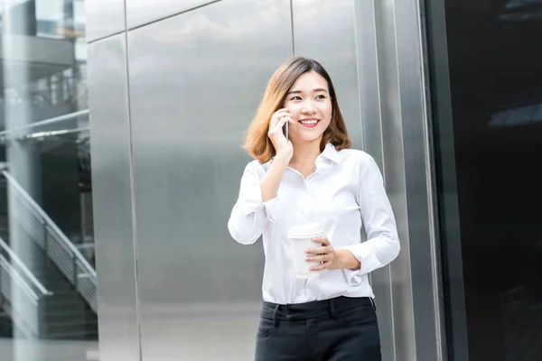 Ασιατικές γυναίκα, καλώντας στο τηλέφωνο κυττάρων μπροστά γραφείο bu — Φωτογραφία Αρχείου