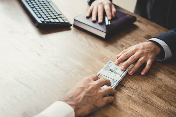 Бизнесмены передают деньги на рабочий стол
 