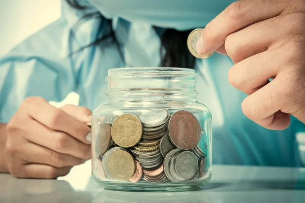 Mano poniendo dinero (moneda) en el frasco de vidrio — Foto de Stock