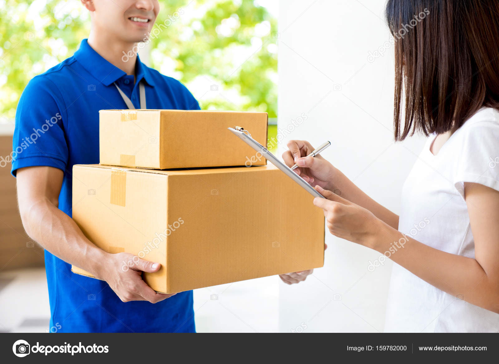 Woman signing document, receiving parcel box from delivery man Stock