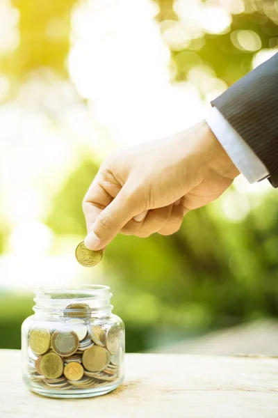 Üzletember kéz a pohárba jar a napokban pénzt (jelentése: érme) — Stock Fotó