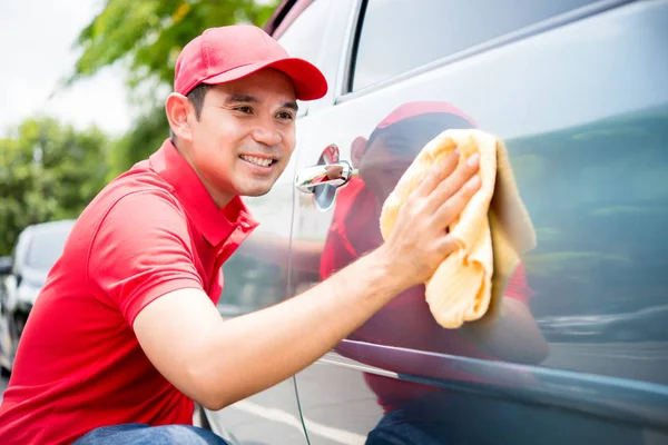Un hombre con uniforme rojo limpiando el coche — Foto de Stock