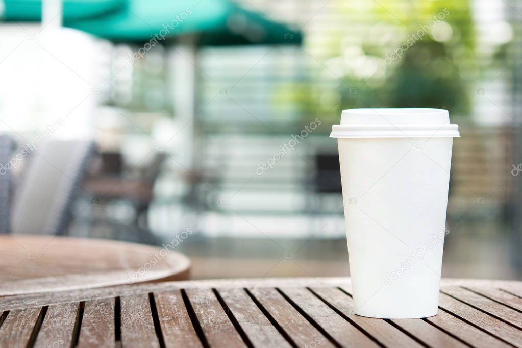 White paper coffee cup on wood table in outdoor cafe