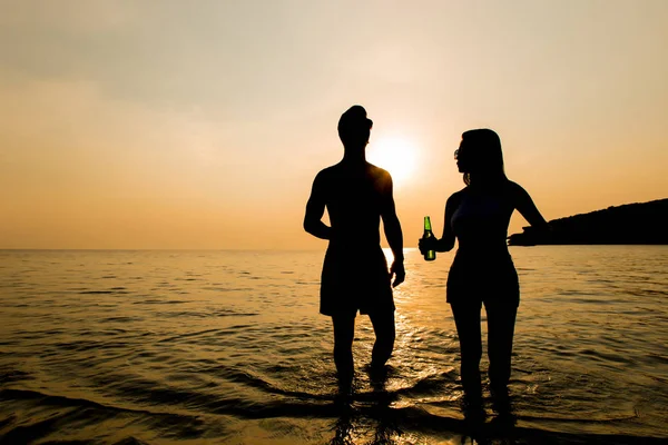 Silhouette of couple walking in seawater at the beach in sunset — Stock Photo, Image