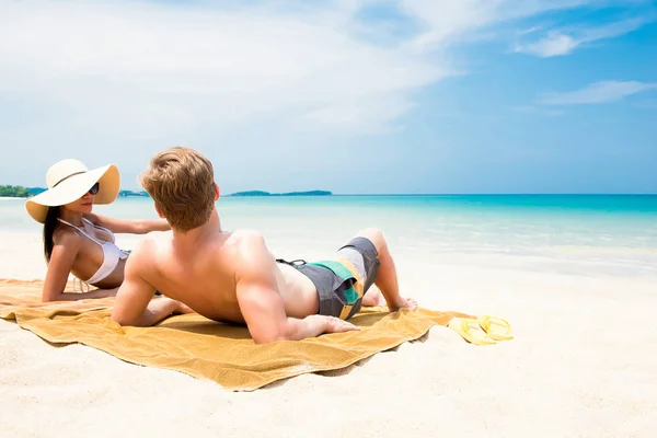 Пара лежить на пляжі з білим піском, розслабляючись і приймаючи сонячну ванну — стокове фото