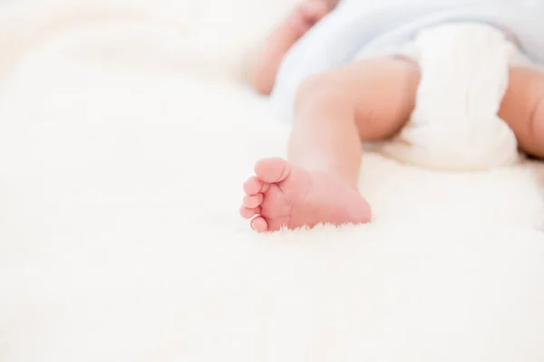 Маленькая ножка новорожденного ребенка на мягкой белой шерстяной простыне — стоковое фото