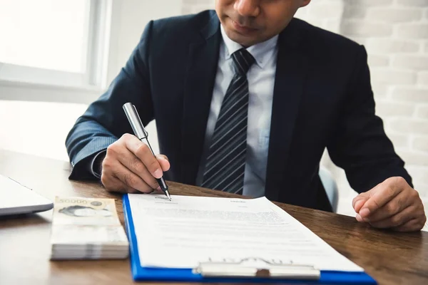 Un homme d'affaires signe un contrat avec de l'argent sur la table — Photo