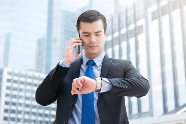 Zakenman zijn horloge kijken terwijl het beroep op cellphone — Stockfoto