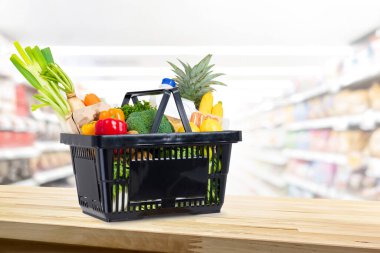 Marketin arka planında, ahşap tezgahın üzerinde alışveriş sepeti dolusu yiyecek.
