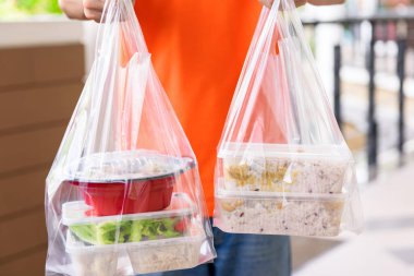 Turuncu üniformalı teslimatçı tarafından evdeki müşterilere plastik poşetlerde Asya yemek kutuları dağıtılıyor.
