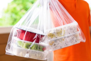 Turuncu üniformalı teslimatçı tarafından evdeki müşterilere plastik poşetlerde Asya yemek kutuları dağıtılıyor.