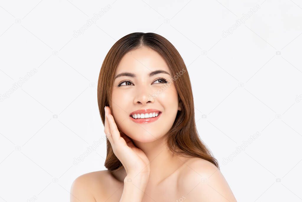 Cheerful beautiful smiling Asian woman with clear fair skin doing hand touching face pose while looking up in white isolated background