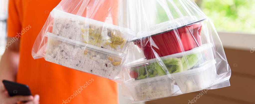 Panoramic banner image of Asian food boxes in plastic bags delivered to customer at home by delivery man