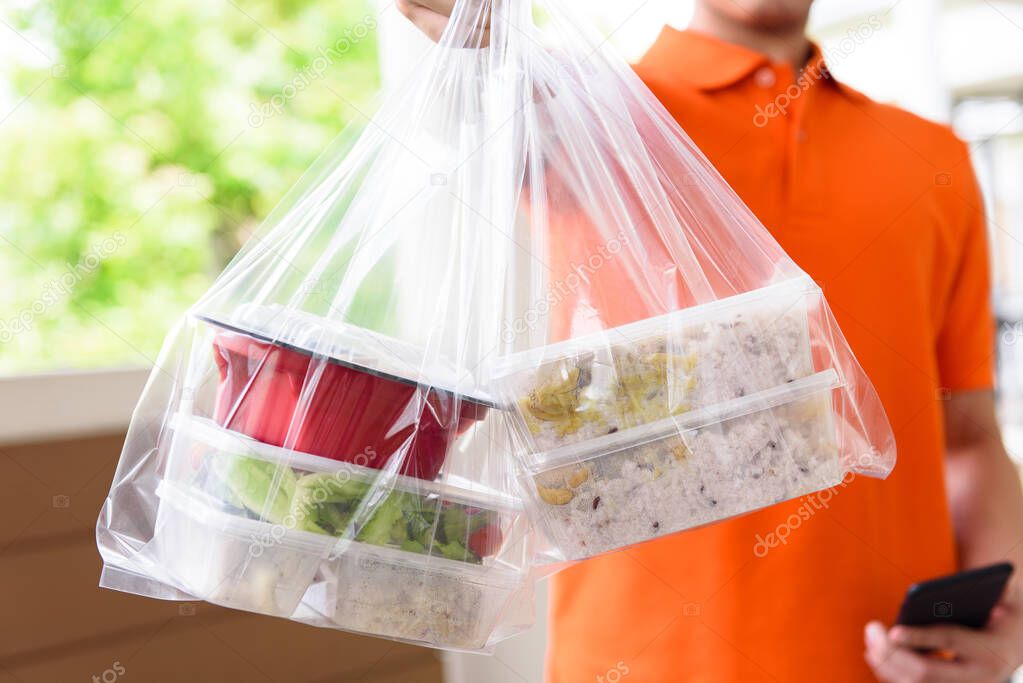 Asian food in take away boxes delivered to customer at home by delivery man in orange uniform