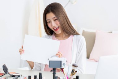 Gülümseyen Asyalı genç kadın güzellik etkileyicisi, mesajlarınız için beyaz kağıtlı bir yer göstererek izleyicilerle iletişim kuruyor.