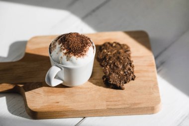 Cup of Babyccino with dark chocolate cookies served on wood platter in cafe clipart