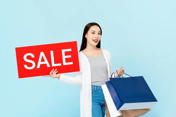 Leende Asiatisk Kvinna Bär Shoppingväskor Visar Röd Försäljning Tecken Ljusblå — Stockfoto