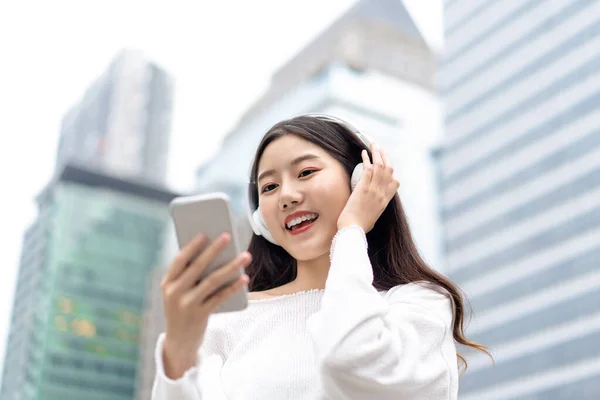Χαρούμενη Χαμογελαστή Ασιάτισσα Που Φοράει Ακουστικά Και Κοιτάει Κινητό Της — Φωτογραφία Αρχείου
