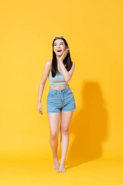Parlak sarı izole stüdyo arka planında avuç içi dokunuşları olan yaz plajı kıyafetli güzel Asyalı kadının tam uzunlukta portresi.