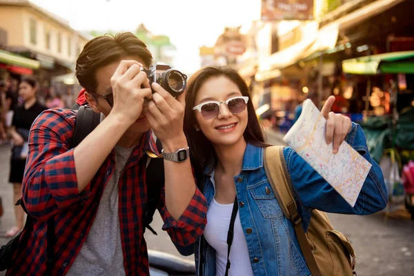 Cheerful young Asian tourist couple taking a photo while happily traveling on Khao San road at Bangkok Thailand