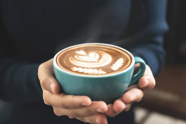 女性の手を保持するコーヒーのカップとともに美しいロゼッタラテアートパターン上の表面 — ストック写真