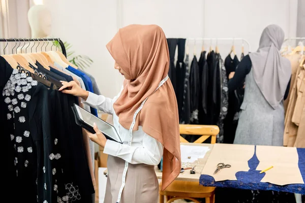 Kobieta Muzułmanin Projektant Gospodarstwa Tablet Podczas Sprawdzania Wieszane Ubrania Sklepie — Zdjęcie stockowe