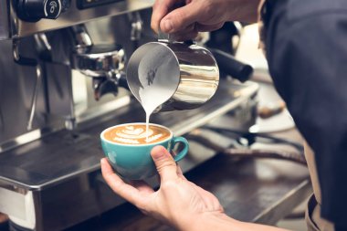 Kahve bardağına buğulanmış süt döken profesyonel barista güzel bir latte sanatı Rosetta deseni yapıyor.